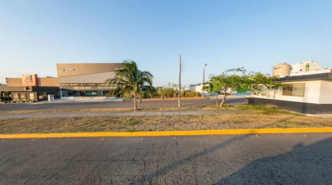 Vista a nivel de calle del corredor comercial donde se ubica el terreno, con agencia automotriz y locales al frente